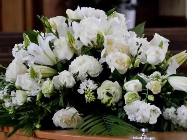 Un arreglo floral blanco sobre un ataúd, con lirios, rosas y otras flores. Estas flores para difuntos simbolizan paz y pureza en el adiós.