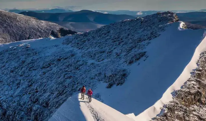 Två vandrare på en snöig bergskam, redo att bestiga Kebnekaise. Vacker utsikt över fjällen.