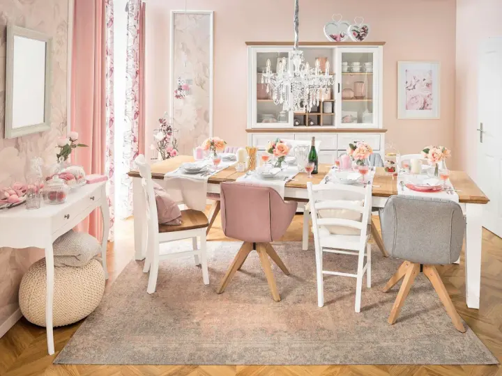 Ein Esstisch im Cottagecore-Stil, gedeckt mit Blumen und rosafarbenen Akzenten. Ein Kronleuchter hängt über dem Tisch.