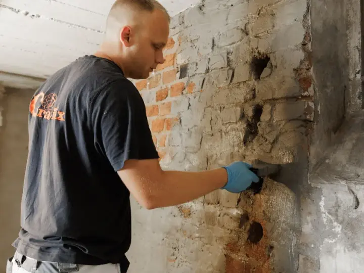 Mann verputzt feuchten Kellerwand.