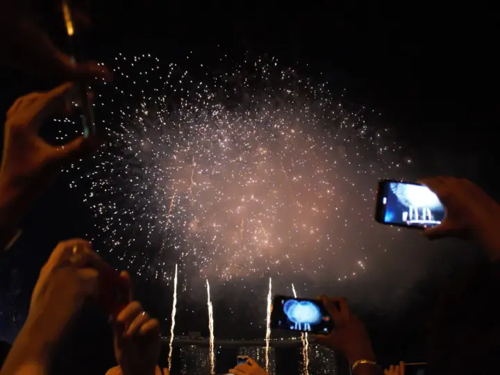 Des mains filment un magnifique feu d'artifice dans le ciel nocturne, capturant la magie de l'instant.