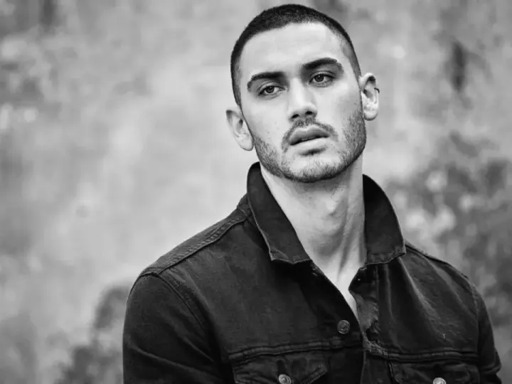 Hombre joven con un corte de pelo buzz cut, viste chaqueta vaquera oscura. Mirada intensa.