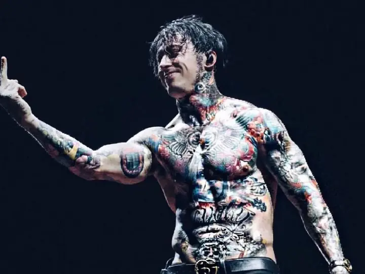 Le chanteur de Falling In Reverse, Ronnie Radke, torse nu et couvert de tatouages colorés, lève le majeur sur scène.