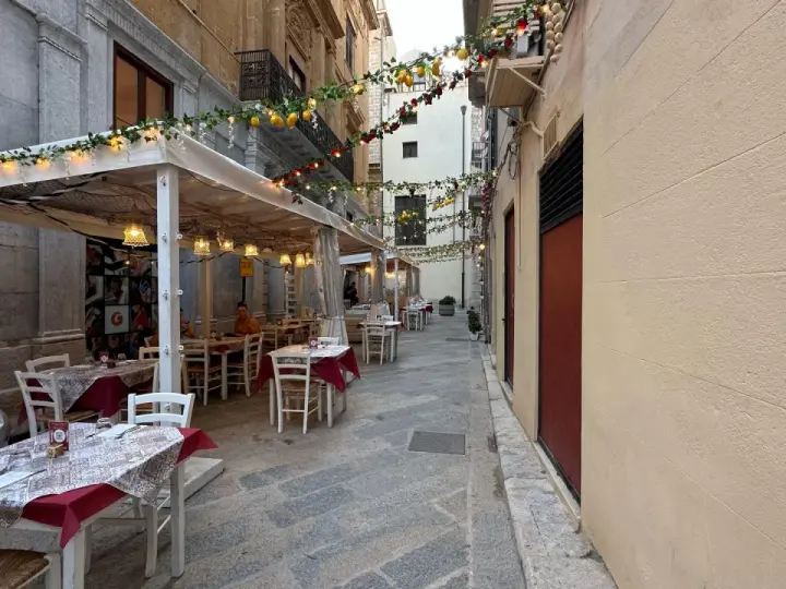 Urocza uliczka w Trapani, gdzie zjeść? Stoliki restauracyjne pod girlandami z cytryn i lampek, idealne na wieczorny posiłek.