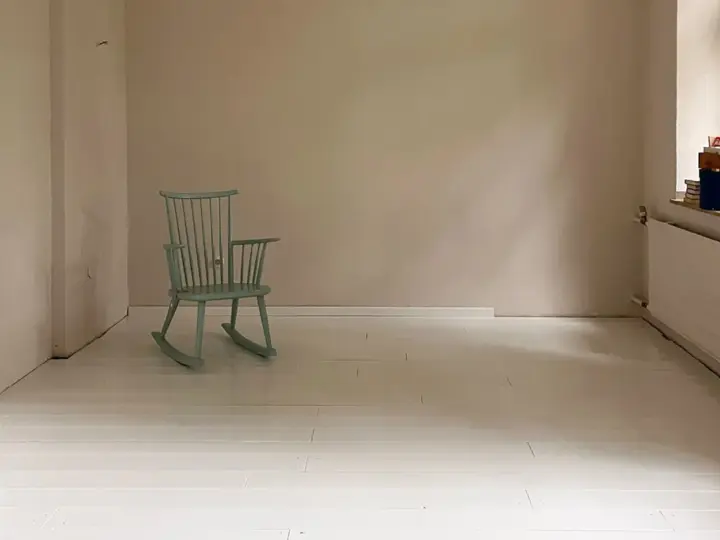 Ein hell gestrichener holzboden mit einer mintgrünen Schaukelstuhl.