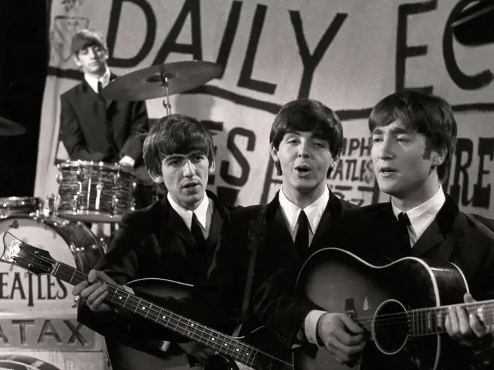 Les Beatles, le groupe le plus connu au monde, jouent sur scène. John Lennon et Paul McCartney chantent, George Harrison joue de la basse, Ringo Starr est à la batterie.