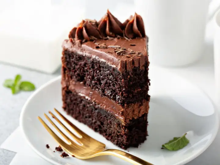 Rebanada de tarta de chocolate con glaseado cremoso y virutas de chocolate. Un tenedor dorado espera pacientemente para probar este delicioso postre.