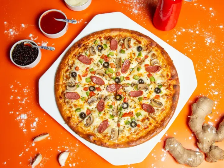 Gotowa pizza z kiełbasą, pieczarkami i papryką, obok sosy i imbir – idealne składniki na pizzę.