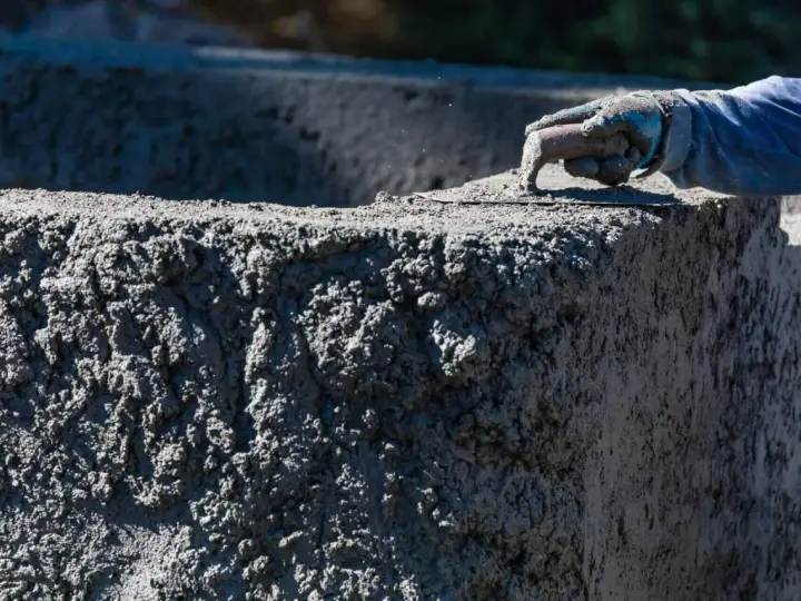 Ręka w rękawicy wygładza świeży beton. Zastanawiasz się, ile kosztuje worek cementu na budowie?