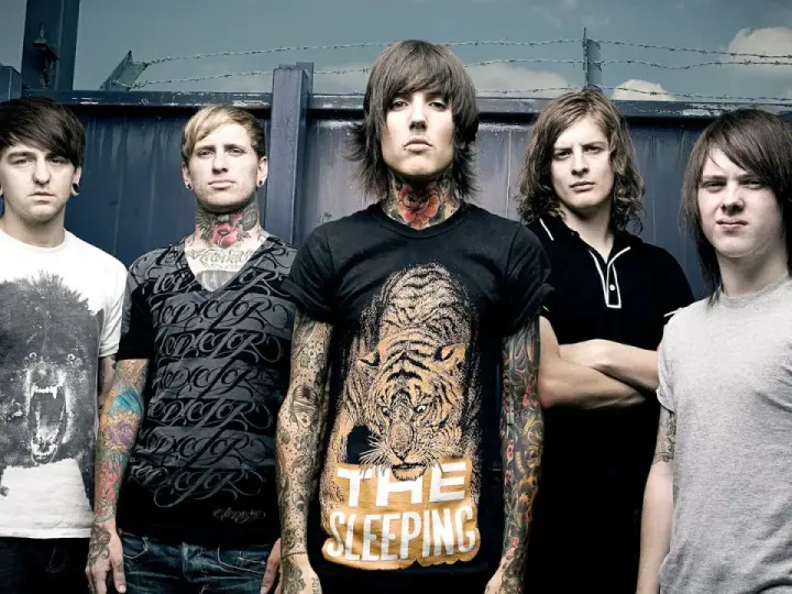 Cinq membres du groupe Bring Me The Horizon posent devant une clôture. Le chanteur porte un t-shirt avec un tigre et le texte "The Sleeping".
