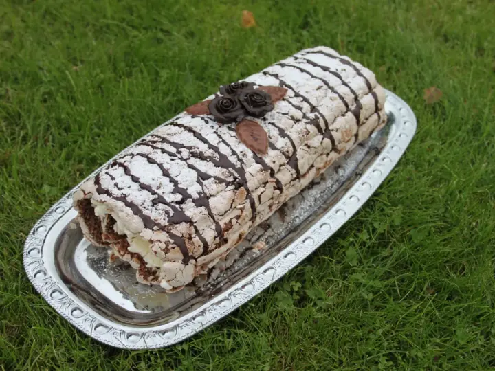 En läcker Budapestrulle med choklad och grädde, dekorerad med chokladrosor och pudersocker. Perfekt för ett sommarfika!