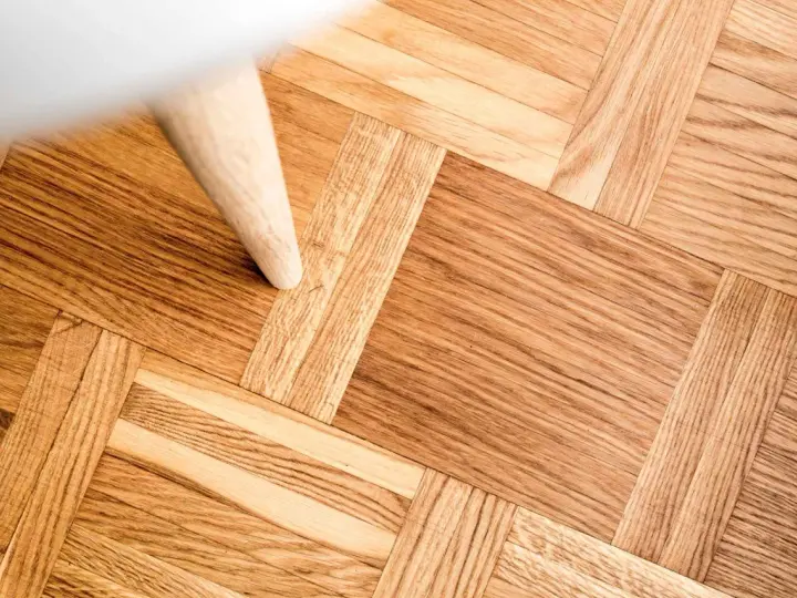 Ett vackert parkettgolv i ek, redo för renovering. En vit möbel står på golvet.