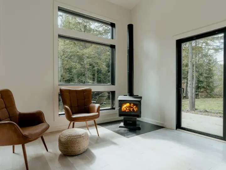 Un poêle à granule appartement, avec deux fauteuils en cuir marron et une vue sur la forêt.