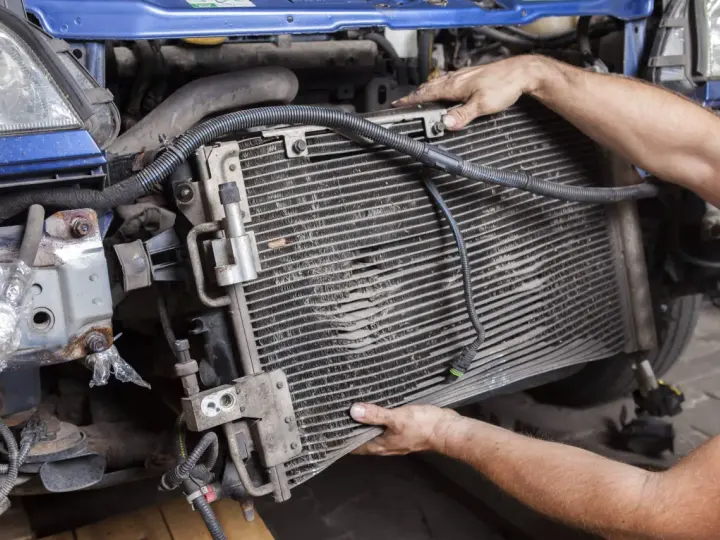 Mechanic removing a car's AC condenser, which blows hot air, for repair.