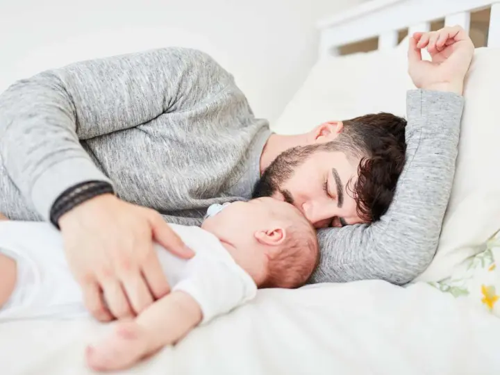 Padre e neonato nel lettone in sicurezza, un momento di dolce riposo e amore.