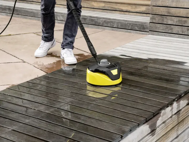 Nettoyage d'une terrasse en bois avec un karcher. L'appareil jaune et noir nettoie le bois sombre, laissant une surface plus claire et humide.