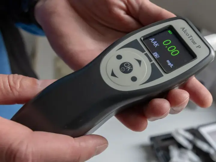 Hände halten ein Alkoholtestgerät, das 0.00 mg/L anzeigt. So vermeidet man eine Strafe wegen Alkohol am Steuer.