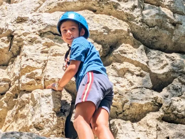 Enfant souriant escaladant un rocher avec un casque bleu.