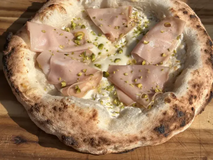 Frisch gebackener Pizzateig mit Mortadella und Pistazien. Ein Genuss, der das Pizzabacken zu einem Erlebnis macht.