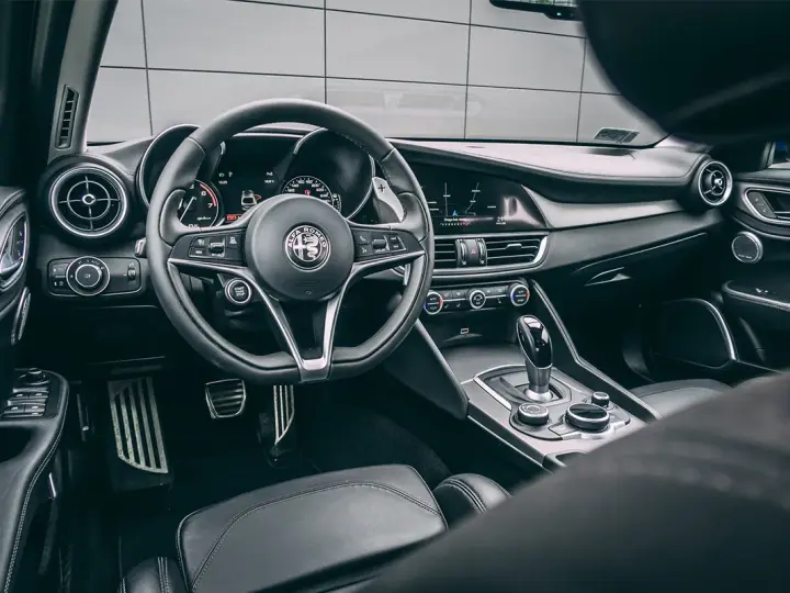 Wnętrze luksusowego samochodu Alfa Romeo. Kierownica, deska rozdzielcza i dźwignia zmiany biegów. Ta fotografia samochodowa oddaje styl i komfort.