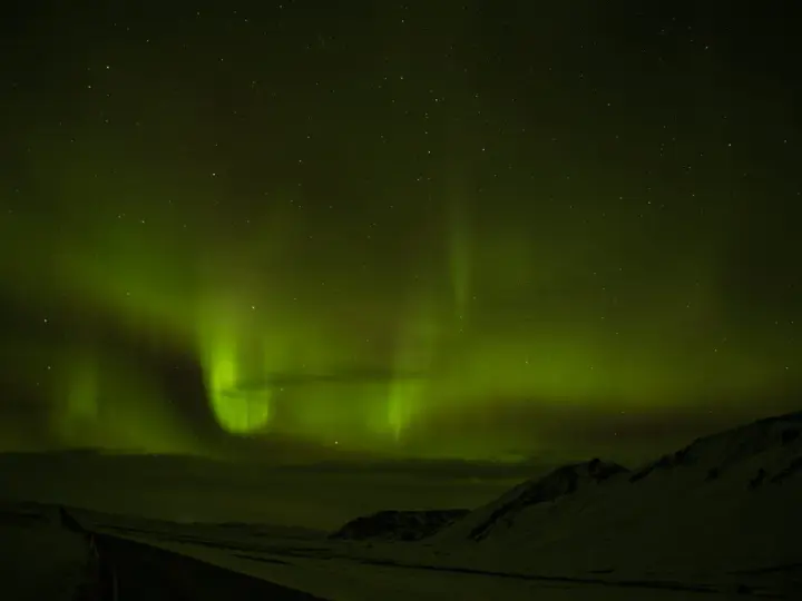 Niesamowita zorza polarna nad Islandią. Zielone smugi tańczą na nocnym niebie, oświetlając ośnieżony krajobraz i drogę.
