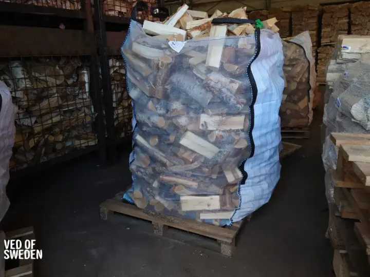 Stor säck med ved på pall, redo att stapla. Veden är kluven och förpackad för leverans.
