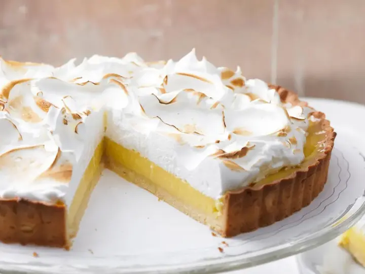 Eine köstliche Tarte au Citron mit fluffiger Baiserhaube, die auf einem Tortenständer präsentiert wird.