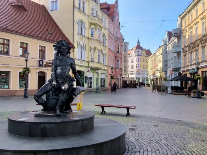 Fontanna z postacią Baccha na brukowanym placu, otoczona kolorowymi kamienicami. Zielona Góra atrakcje turystyczne.