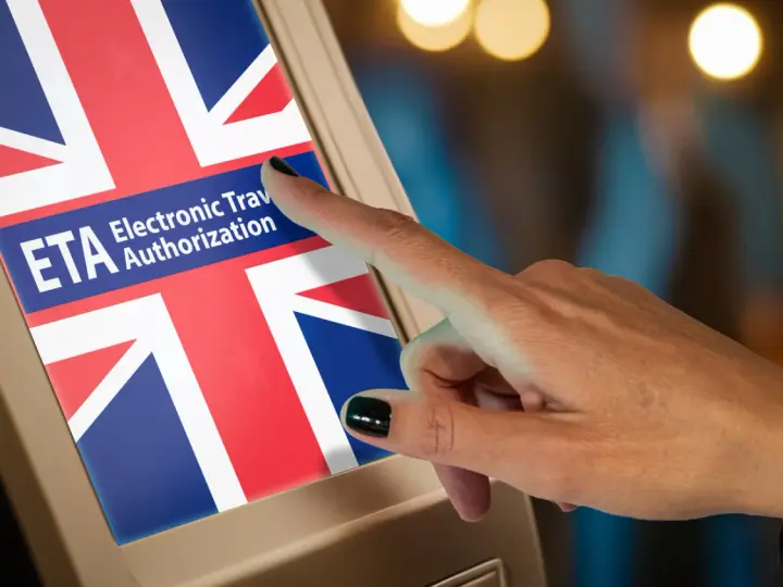 Dłoń dotyka ekranu z flagą Wielkiej Brytanii i napisem ETA. Czy do Wielkiej Brytanii potrzebny jest paszport? ETA to elektroniczne zezwolenie na podróż.