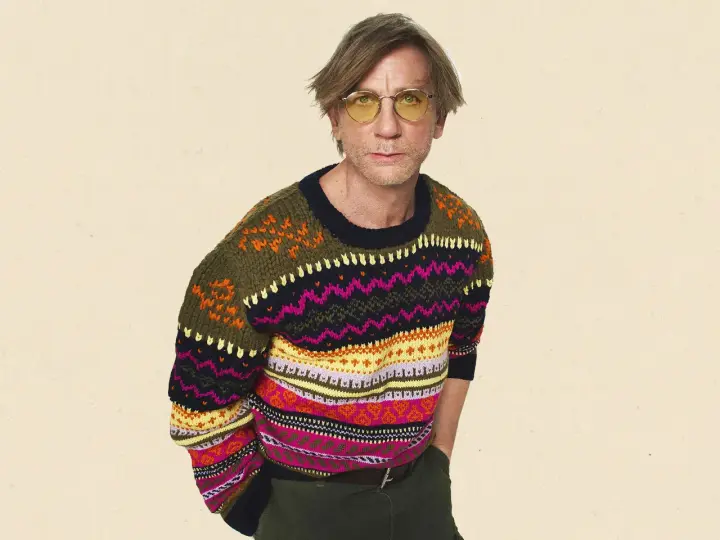 Mann mit gelber Brille trägt einen bunten Pullover aus Wolle, schleudern von Mustern.