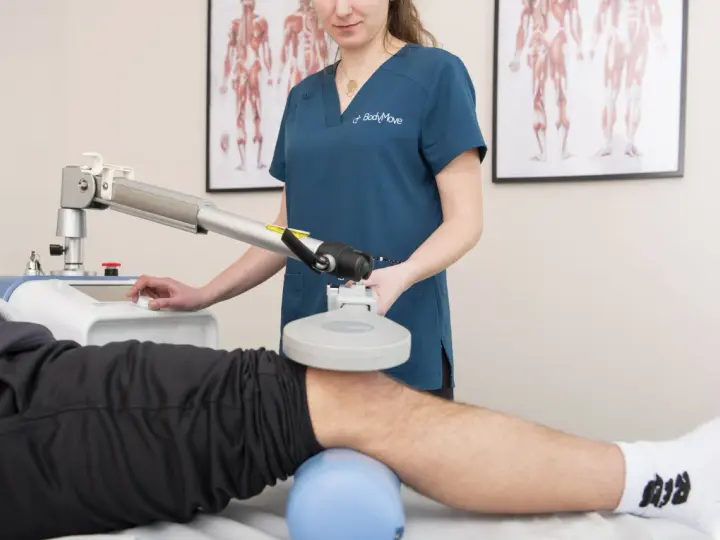 Fizjoterapeuta wykonuje zabieg rehabilitacyjny na kolanie pacjenta za pomocą specjalistycznego urządzenia.