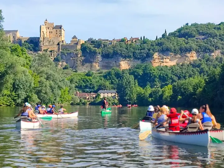 Des gens en canoë sur une rivière, avec un château en arrière-plan.