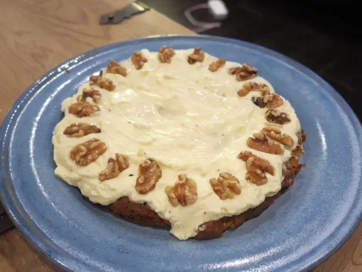 En saftig glutenfri morotskaka med krämig frosting och valnötter på en blå tallrik.