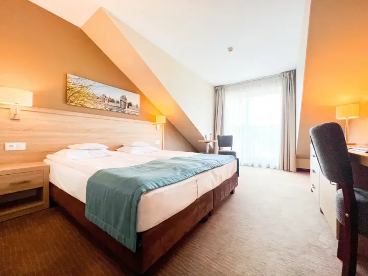 Przytulny pokój hotelowy z wygodnym łóżkiem, biurkiem i oknem. Idealne miejsce na nocleg tranzytowy, by odpocząć w podróży.