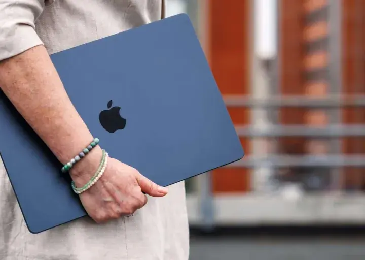 Donna con un MacBook blu, logo Apple visibile. La pulizia del mac è evidente, pronto per nuove avventure.