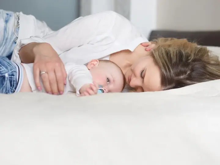 Mama tuli tuląca dziecko, ucząc się jak odkładać dziecko do łóżeczka, by spało spokojnie.