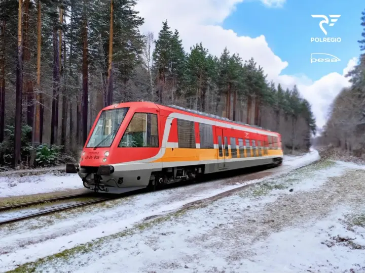 Czerwono-żółty pociąg EN 81-005 Polregio mknie przez zaśnieżony las.