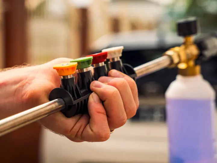 Choosing the right nozzle to pressure wash car is key. This hand holds a selection of colored tips for a pressure washer wand, ready for detailing.
