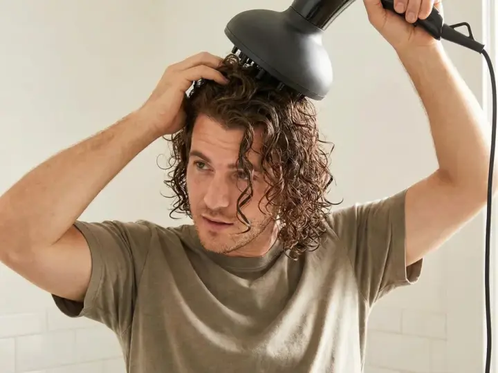 Ein junger Mann mit wellen haaren föhnt sich die Locken mit einem Diffusor.