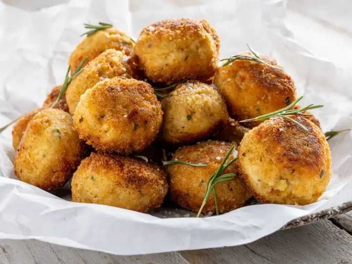 Un mucchio invitante di polpette in bianco, dorate e croccanti, guarnite con rosmarino fresco e sale grosso.