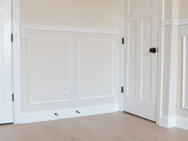 A room with a DIY chair rail, wainscoting, and white doors. The walls are painted a light cream color.
