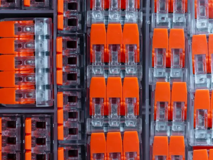 Zbliżenie na pomarańczowe złącza elektryczne w przezroczystych obudowach, ułożone w rzędy.