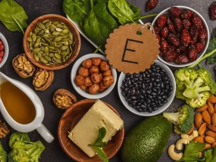 Assortiment d'aliments riches en vitamine E : amandes, noisettes, épinards, avocat, haricots noirs, graines de courge, et huile.