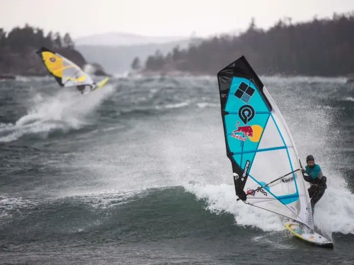 Windsurferzy na falach, jeden z nich na pierwszym planie, w akcji.