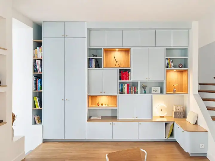 Aménagement d'un **pièce à vivre** moderne avec bibliothèques modulables, rangements intégrés et un banc cosy près de l'escalier.