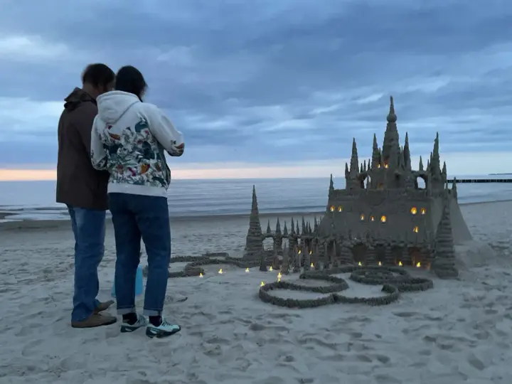 Para podziwia imponujące zamki z piasku na plaży, w okolicach Kołobrzegu. Wieczorne światła dodają magii.