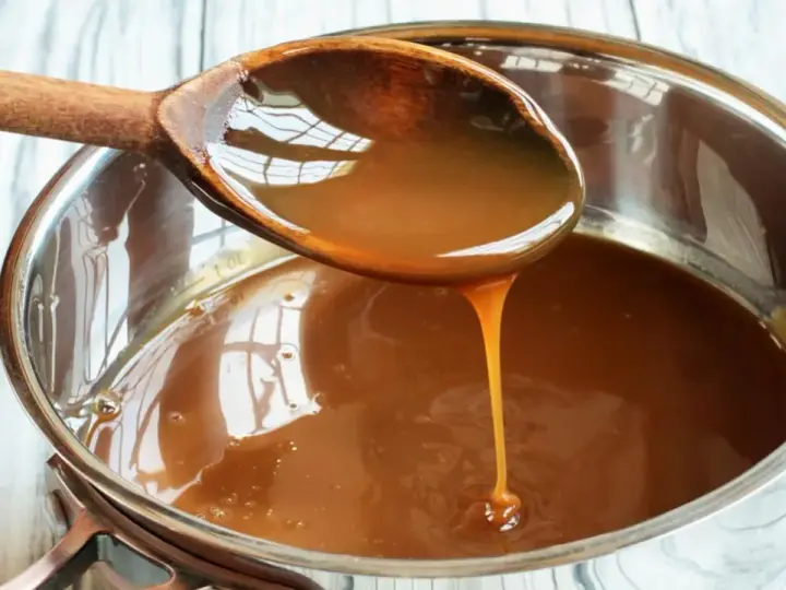 Caramelo líquido cayendo de una cuchara de madera a una olla, perfecto para tu flan al estilo Eva Arguiñano.