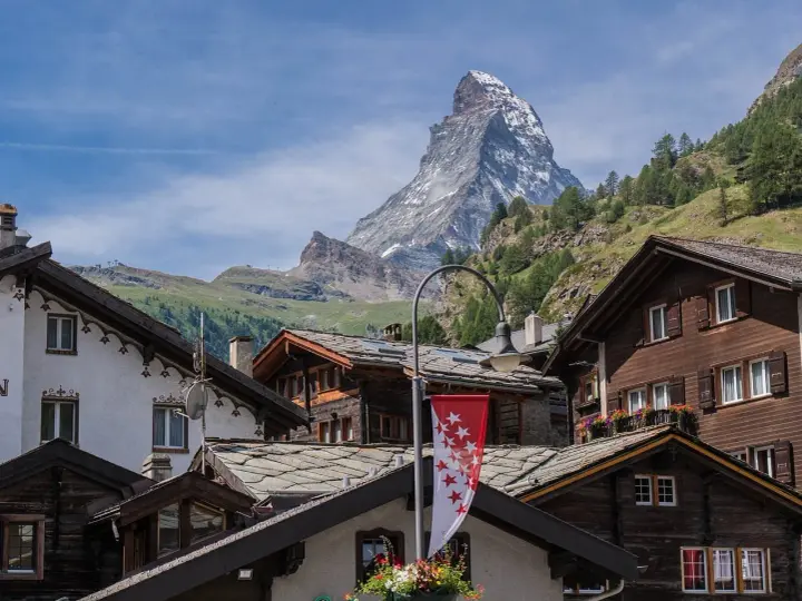 Tradycyjna winieta szwajcaria: drewniane domy z kamiennymi dachami i majestatyczny Matterhorn w tle.