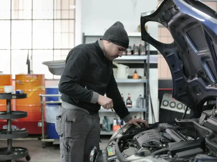 Mechanik w czapce z daszkiem sprawdza silnik. Zastanawiasz się, ile zarabia mechanik? Praca wymaga precyzji i wiedzy.