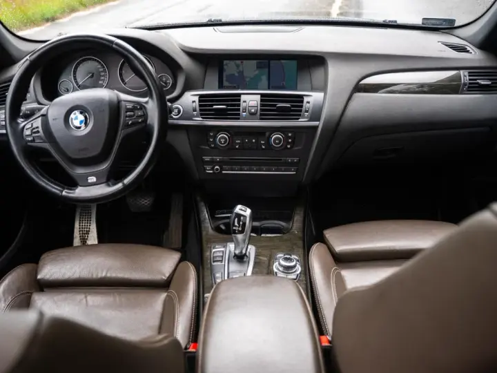Wnętrze BMW X3 z brązową skórzaną tapicerką i drewnianymi wstawkami. Kierownica, deska rozdzielcza i nawigacja. Wiele osób szuka bmw x3 opinie, by poznać ten model.
